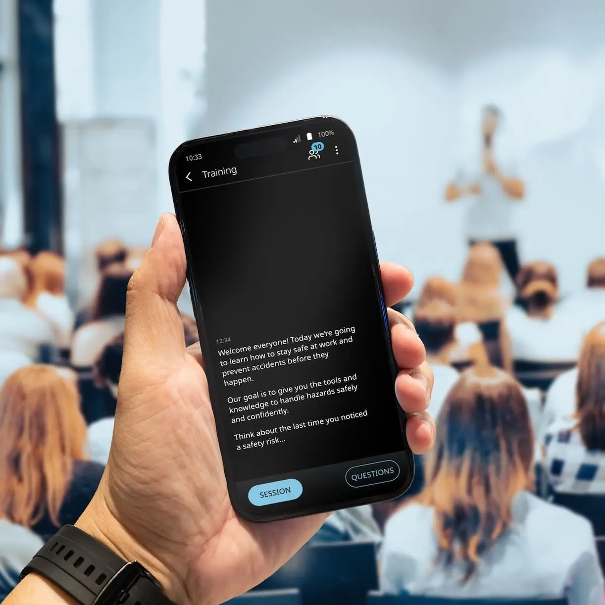 Vasco Audience Numa sala repleta de pessoas, está a decorrer uma palestra. Um homem segura na mão um telemóvel, no qual é exibida uma tradução através do Vasco Audience