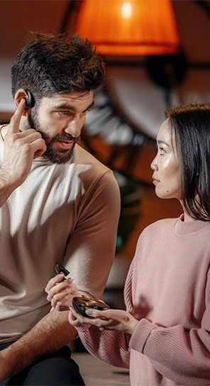 Um homem com o auricular Vasco Translator E1, ao lado de uma mulher que segura o dispositivo E1, exibindo os seus potentes altifalantes e o microfone inteligente.