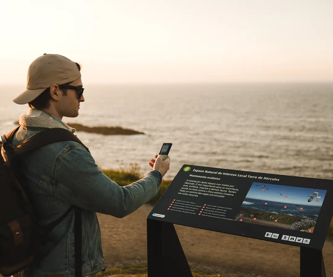 um homem à beira-mar usando um tradutor fotográfico para ler uma placa com informações turísticas sobre a sua localização